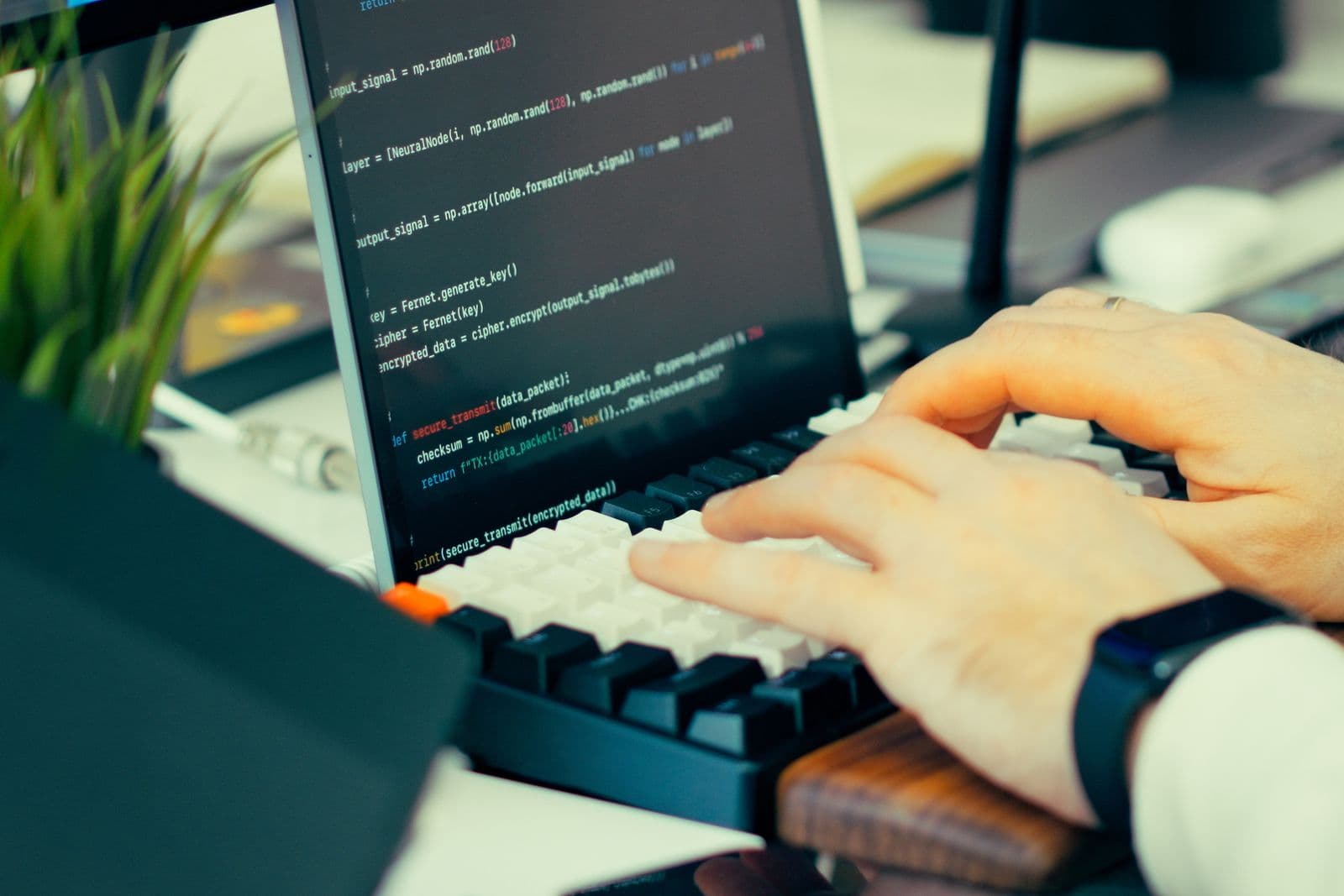 Hands type on a keyboard beside a laptop screen showing code.