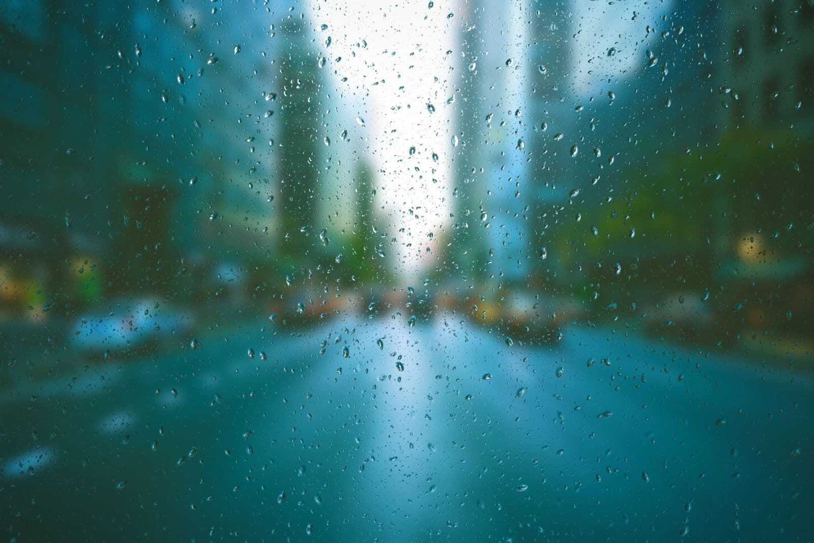 Raindrops on glass with a blurred city street and tall buildings beyond.